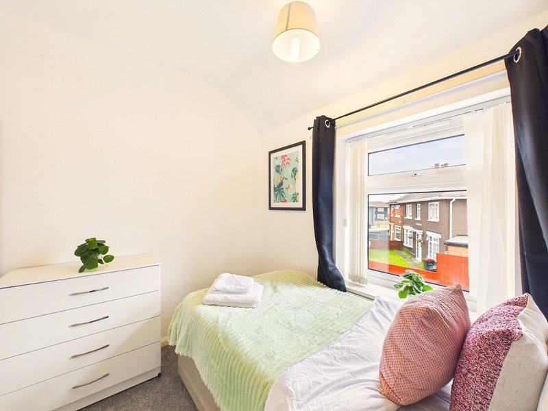 Small bedroom with single bed, white drawers, framed botanical print, and patio door view