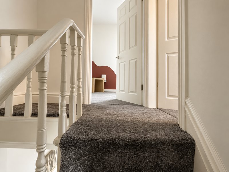 Upstairs hallway with staircase, grey carpet, white doors and cream walls