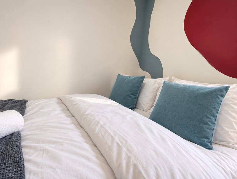 Modern bedroom with white bedding, blue pillows, and abstract wall art