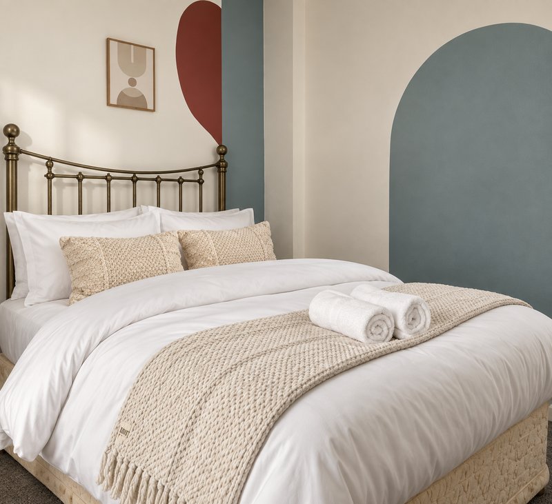 Modern bedroom with brass bed frame, white bedding, beige throw, and geometric wall art