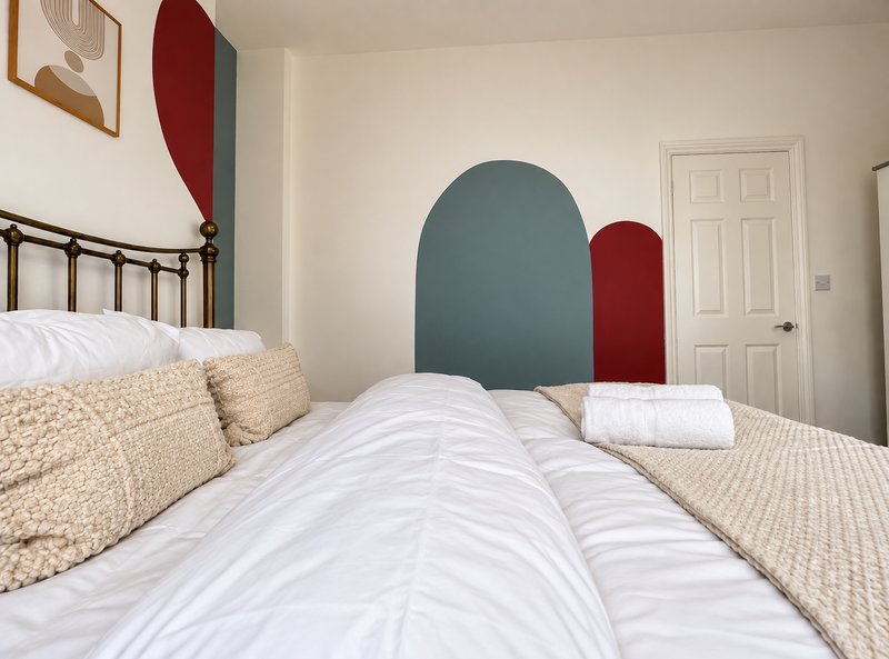 Bedroom with double bed, metal headboard, cream pillows, and geometric wall art