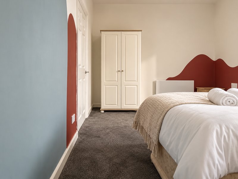 Bedroom with double bed, red headboard, wardrobe, and grey carpet flooring