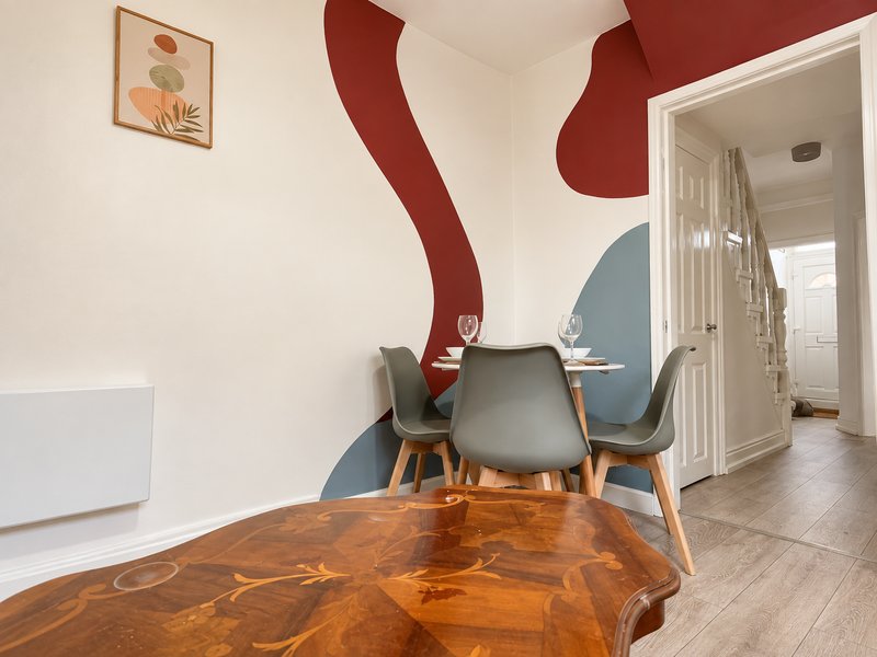 Modern dining area with round wooden table, gray chairs, and red abstract wall art