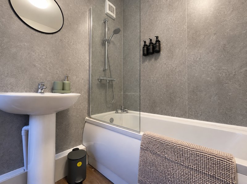 Modern bathroom with pedestal sink, bathtub, glass shower screen, and gray tile walls