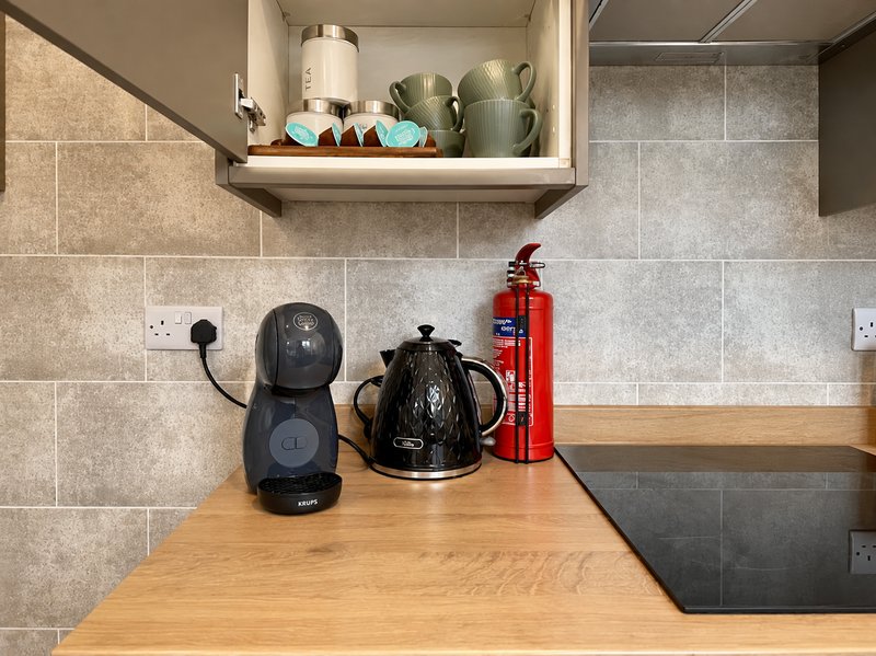 Kitchen countertop with coffee maker, kettle, fire extinguisher and open shelving above