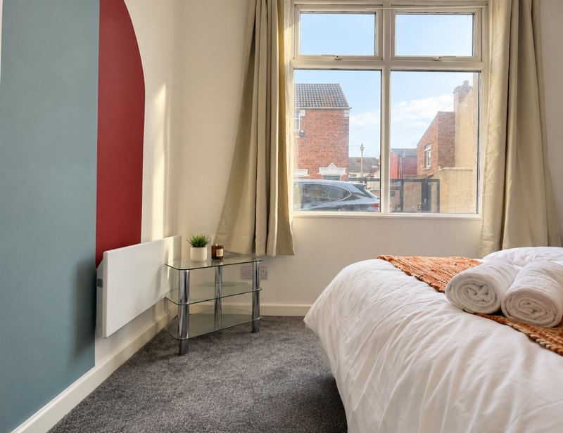 Bedroom with double bed, white bedding, side table, window overlooking brick buildings