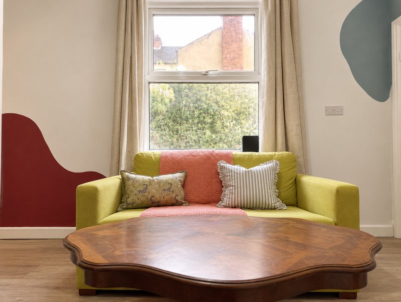 Modern seating area with yellow sofa, colorful cushions, wooden table and large window