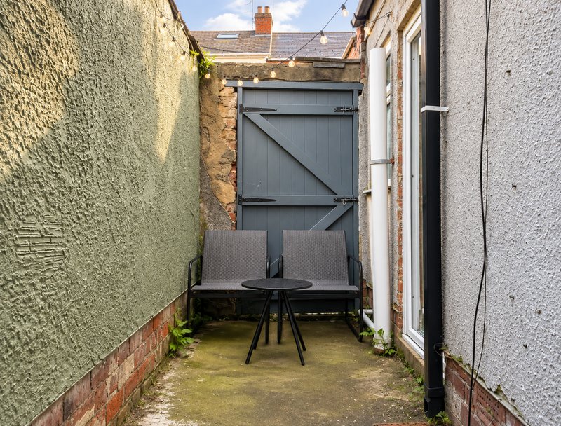 Narrow outdoor courtyard with table, chairs, and surrounding brick walls