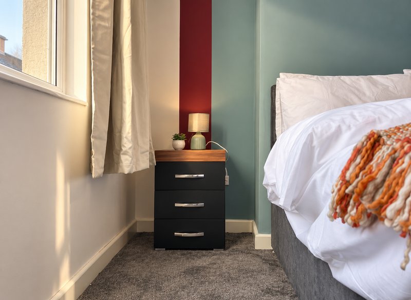 Modern bedroom with double bed, black nightstand, window with curtains, and teal accent wall