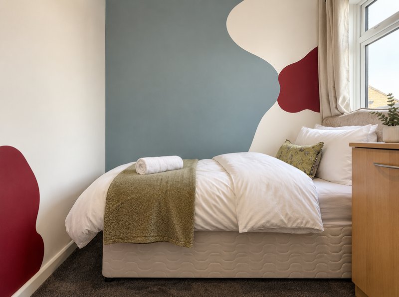 Modern bedroom with double bed, olive throw, white pillows, two-tone wall art and wooden nightstand