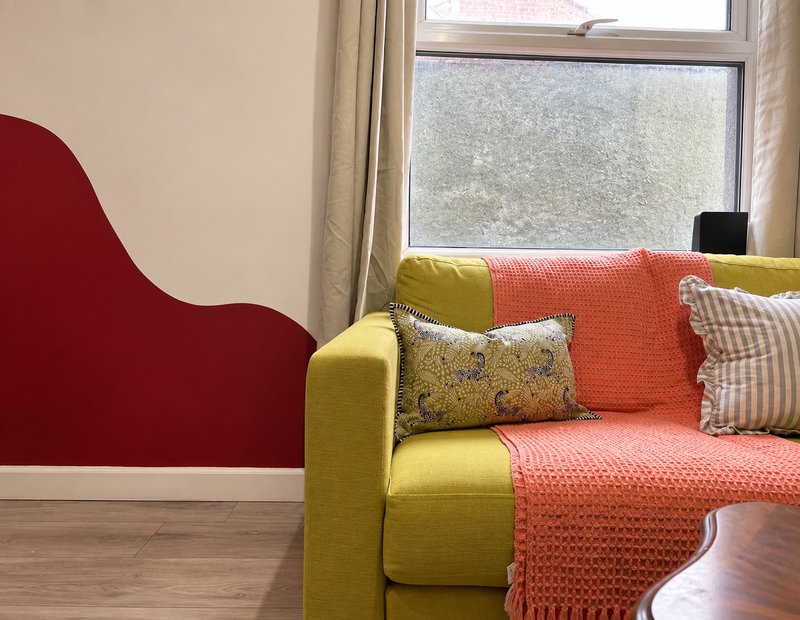 Colorful living room with yellow and orange upholstered sofa, decorative cushions, and window with curtains