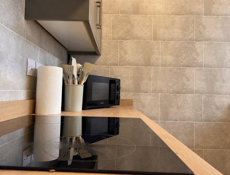 Kitchen counter with microwave, utensil holder, paper towels and tiled backsplash