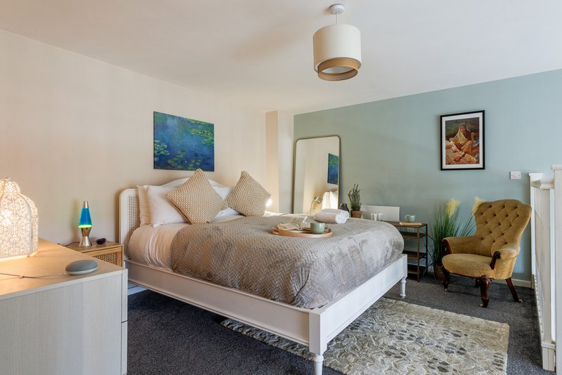 Bright bedroom with double bed, mustard armchair, blue accent wall and pendant light