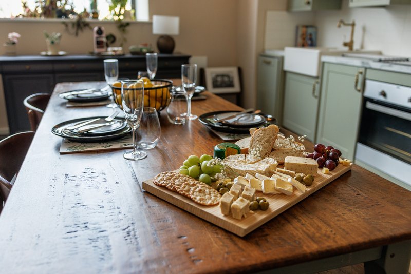 Kitchen dining table set for a meal with cheese board, glasses and place settings