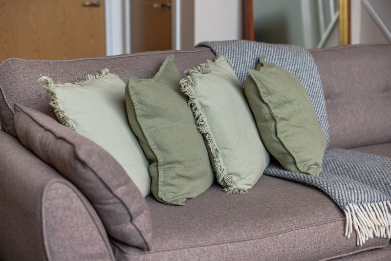 Gray upholstered sofa with green and cream decorative cushions and throw blanket