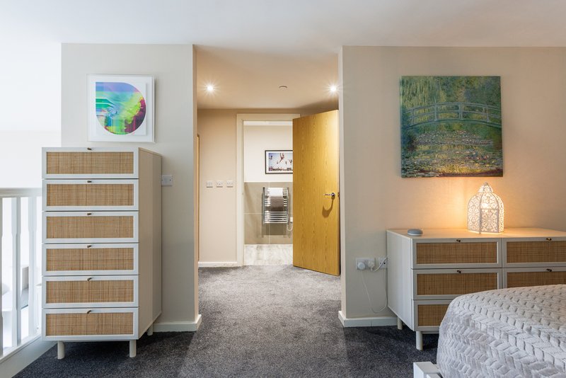 Modern bedroom with wooden storage unit, framed artwork, ensuite bathroom visible through open yellow door
