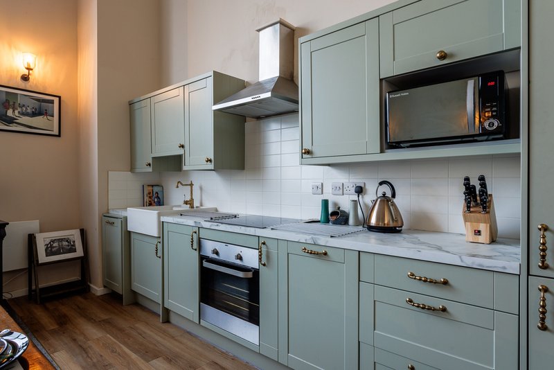 Modern kitchen with sage-green cabinetry, white subway tile backsplash, stainless steel appliances and wooden flooring
