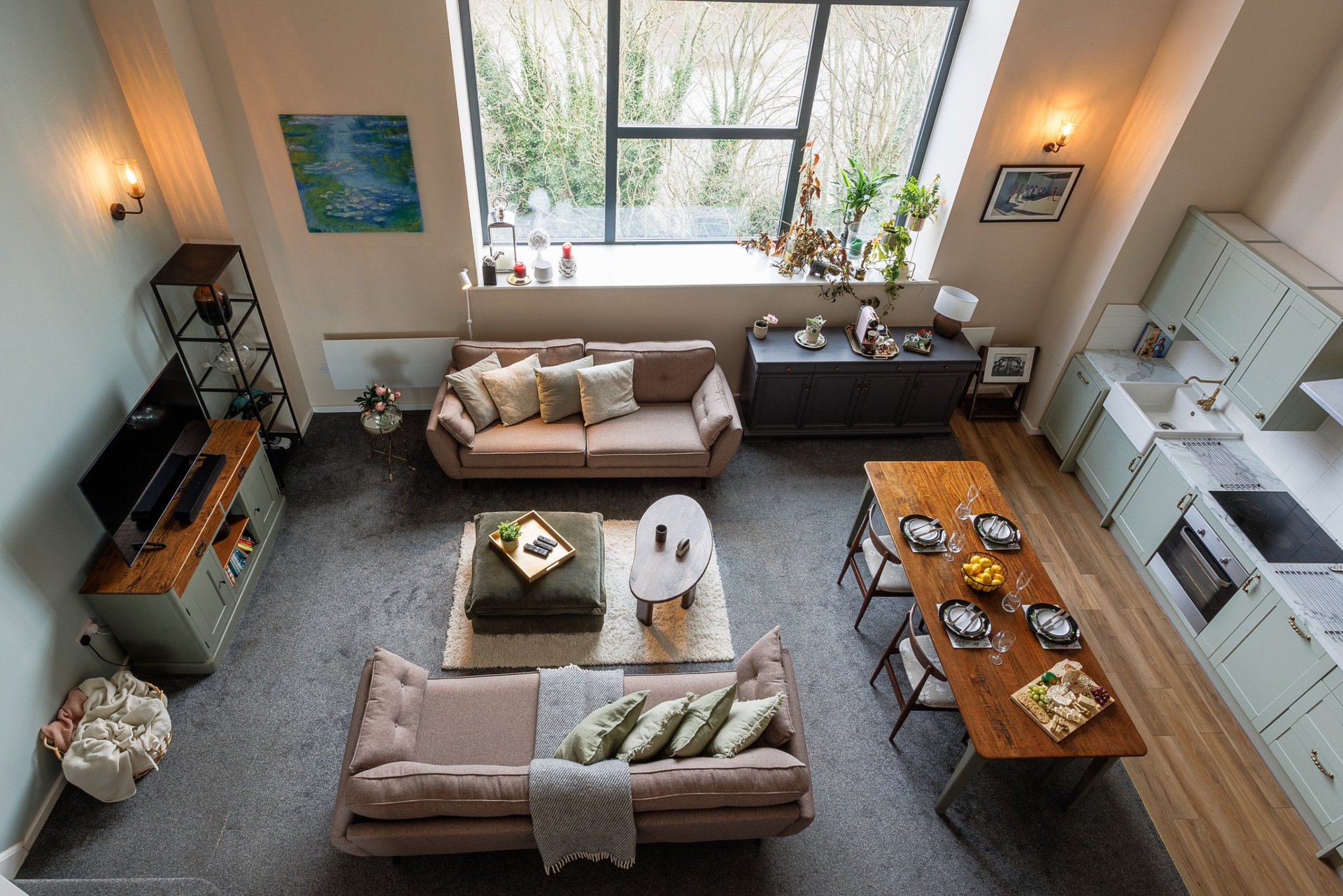 Open-plan living area with sofa, dining table, kitchen, and large windows overlooking garden
