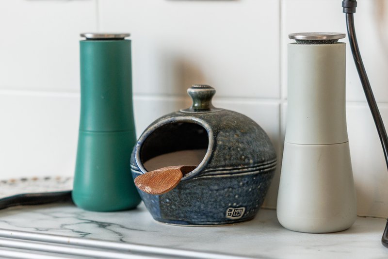 Kitchen counter with teal and cream salt and pepper shakers, dark ceramic teapot, and marble surface