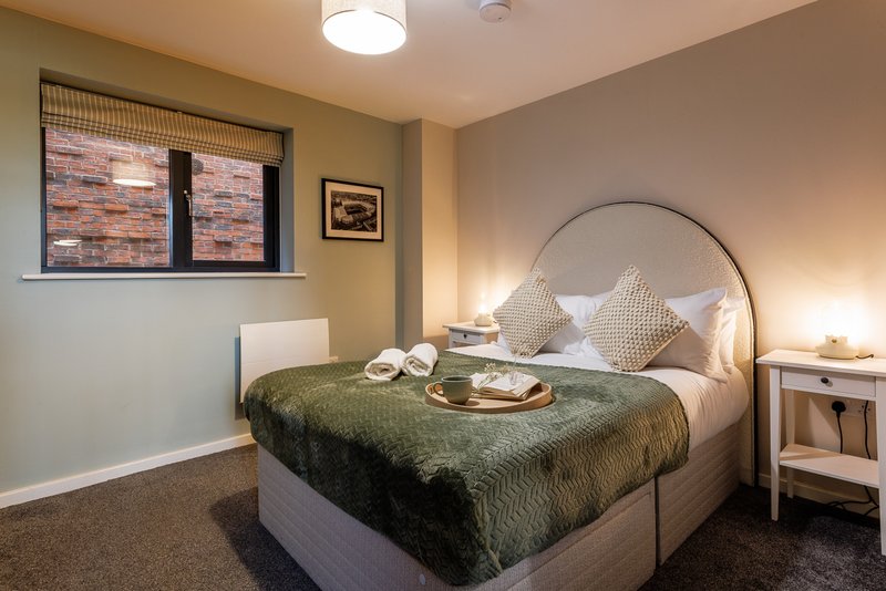 Bedroom with arched metal bed frame, green bedding, white pillows, brick-pattern window, and bedside lamp