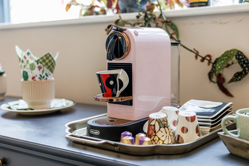 Kitchen counter with pink coffee machine, decorative plants, and tableware on tray