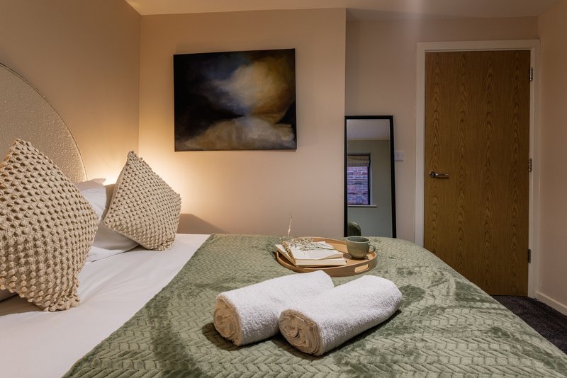 Bedroom with double bed, patterned cushions, rolled towels, and framed artwork on wall