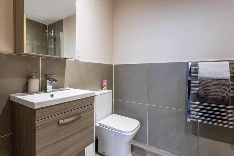 Modern bathroom with vanity sink, toilet, heated towel rail and grey tile walls