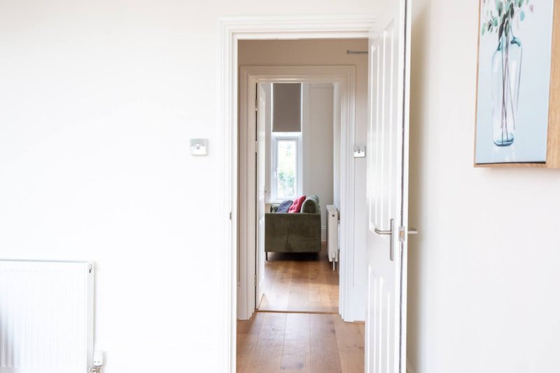 Bright hallway with white doors leading to bedroom, wooden flooring and wall art