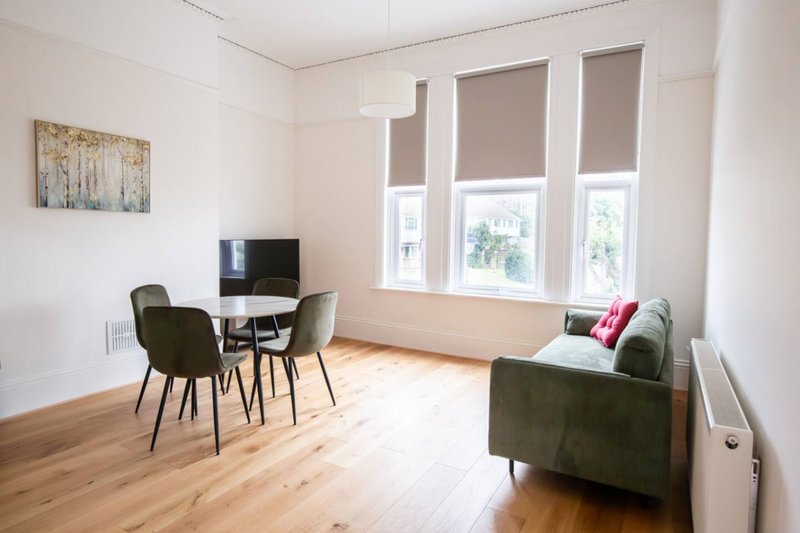 Bright living room with dining table, chairs, sofa and large windows with blinds