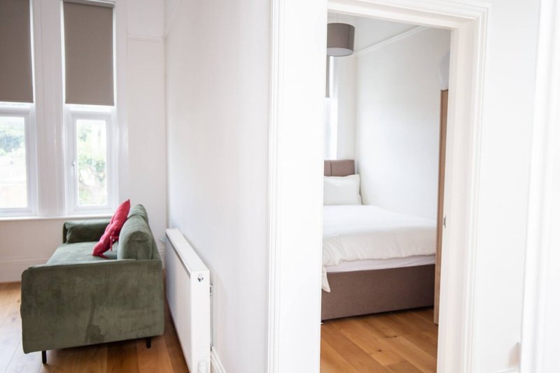 Bright hallway with green armchair, red cushion, and doorway to bedroom with white bedding