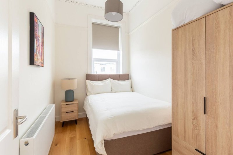 Compact bedroom with double bed, wooden wardrobe, bedside table and window