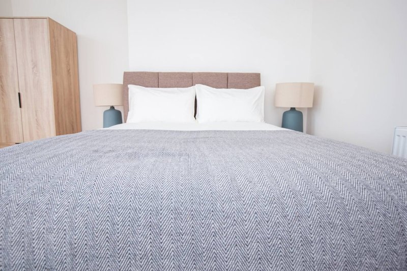 Modern bedroom with double bed, grey bedding, upholstered headboard and wooden wardrobe