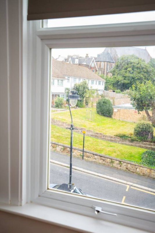 Window view of residential street with neighbouring houses, garden and green trees