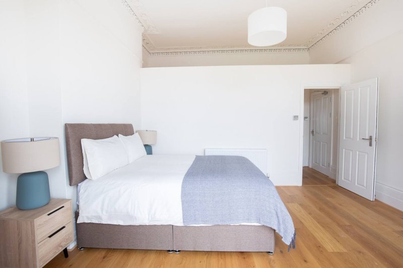 Bright bedroom with double bed, wooden floor, bedside lamp and white wardrobe