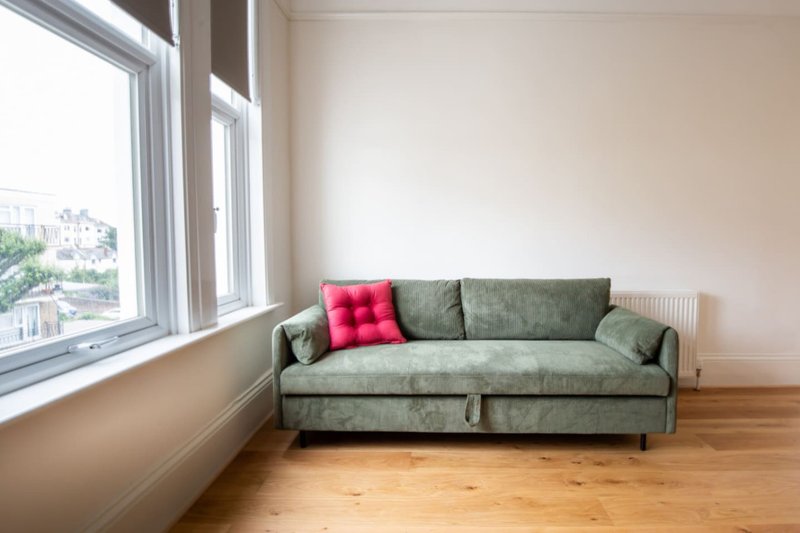 Bright living room with green upholstered sofa, red cushion, wooden floor and large windows