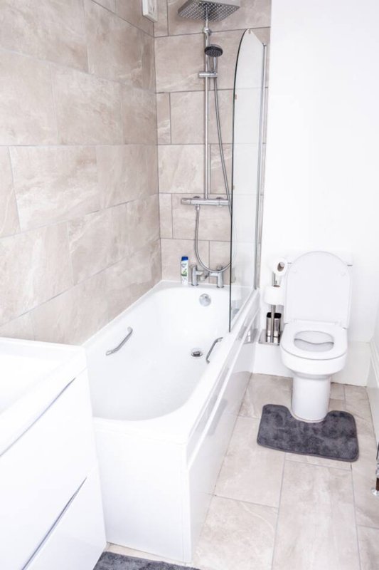 Modern bathroom with white bathtub, shower enclosure, toilet, and beige tile walls
