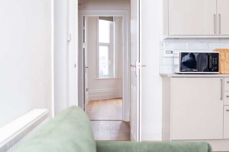 Modern kitchen with white cabinets, microwave, and doorway to hallway with natural light