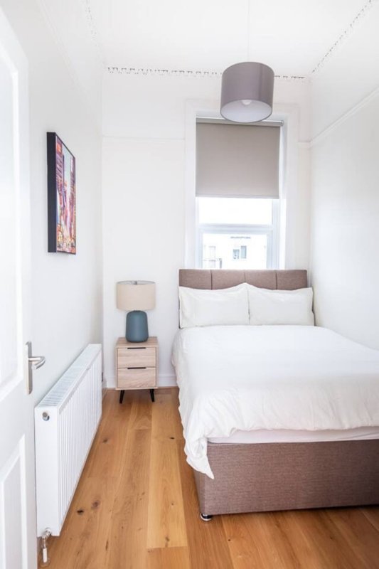 Compact bedroom with double bed, wooden floor, bedside table and window with blind