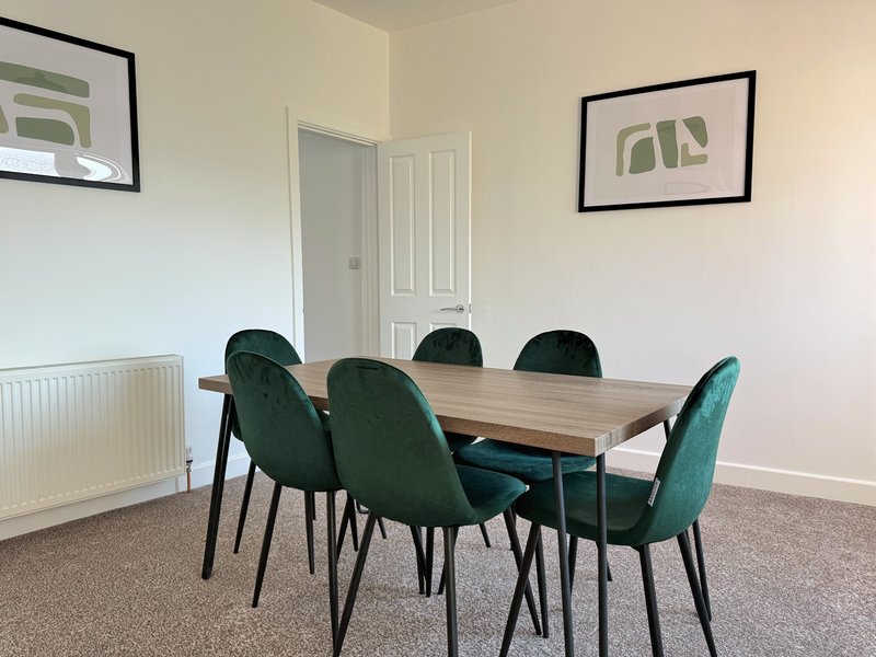 Dining room with wooden table, six green upholstered chairs, and framed wall art