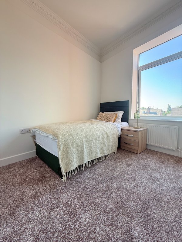 Bright bedroom with single bed, wooden bedside table, large window overlooking city skyline
