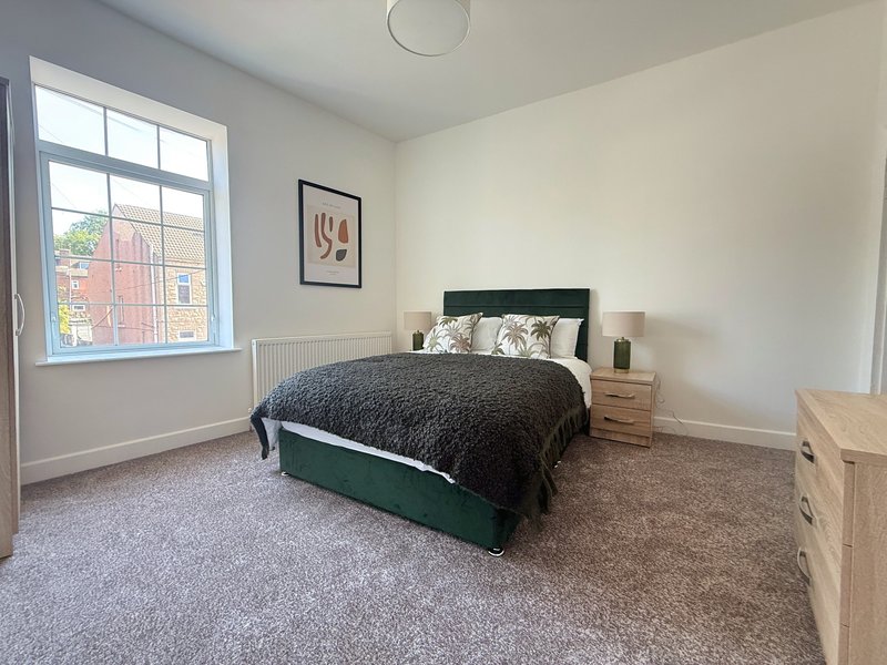 Bright bedroom with green bed frame, wooden nightstands, large window and minimalist wall art