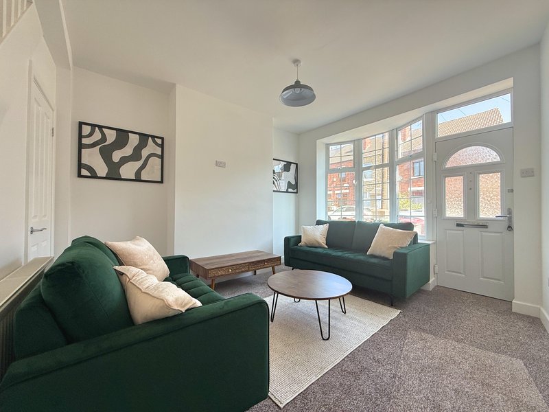 Bright living room with green sofas, coffee table, wall art, and large bay windows