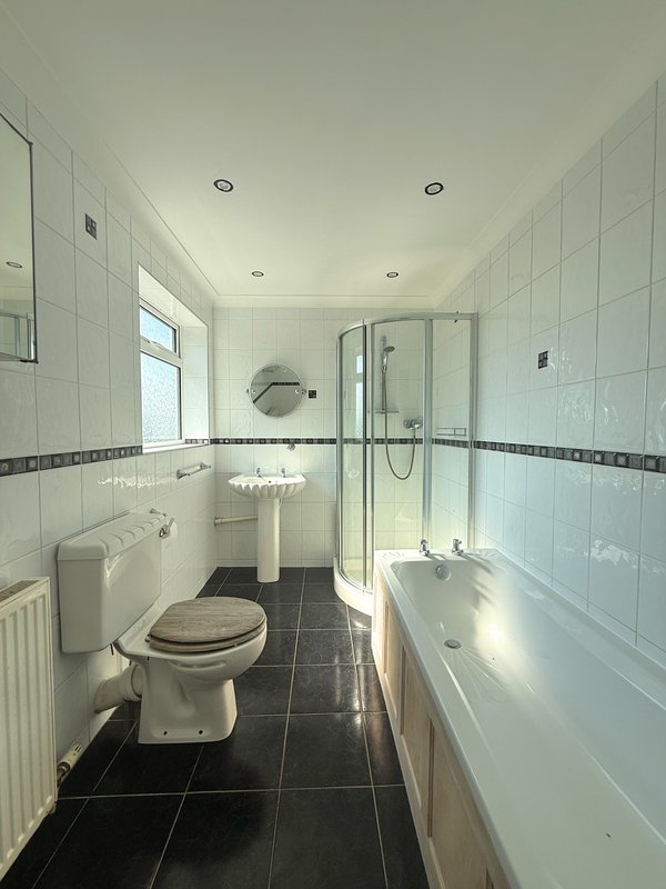 Modern bathroom with white tiles, black floor, toilet, sink, shower cubicle and bathtub