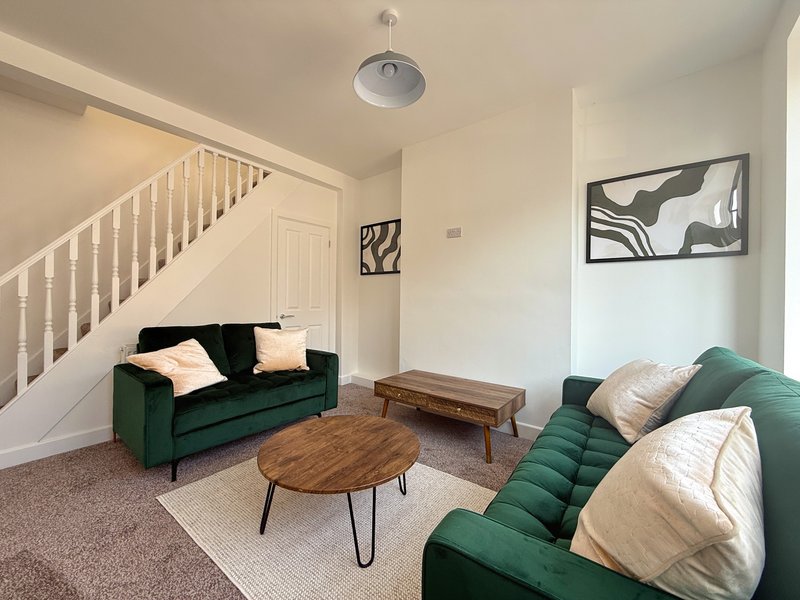 Open-plan living room with green sofas, wooden coffee tables, staircase and framed wall art