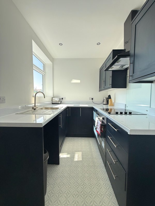 Modern kitchen with dark cabinetry, white countertops, stainless steel appliances and window