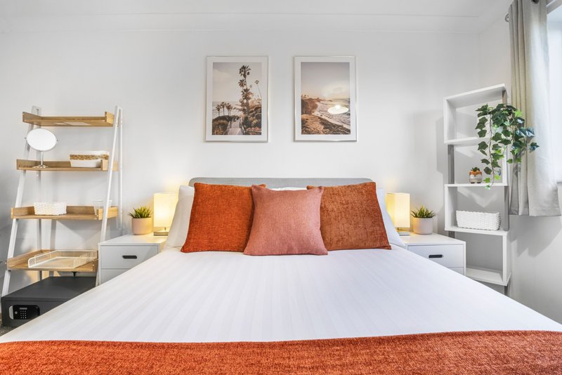 Modern bedroom with white bed, orange and pink cushions, wooden ladder shelf and framed wall art