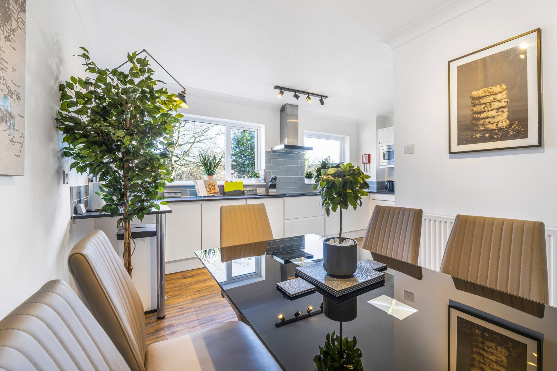 Modern open-plan kitchen and dining area with wooden table, upholstered chairs, plants and pendant lighting