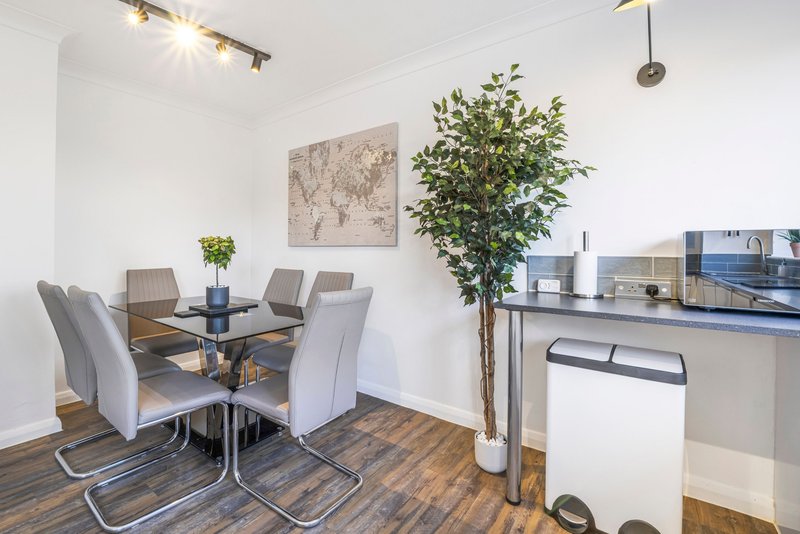 Modern dining area with round glass table, gray upholstered chairs, and potted plant