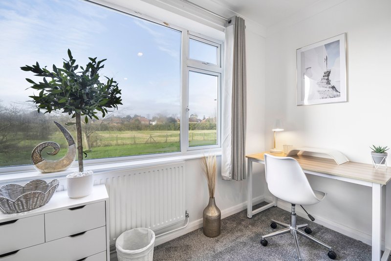 Bright home office with desk, white chair, potted plant and countryside view through window