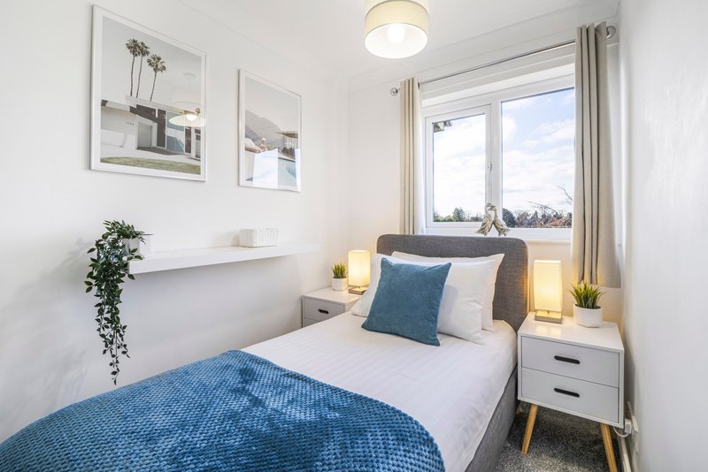 Modern bedroom with single bed, blue bedding, white nightstands and framed wall art